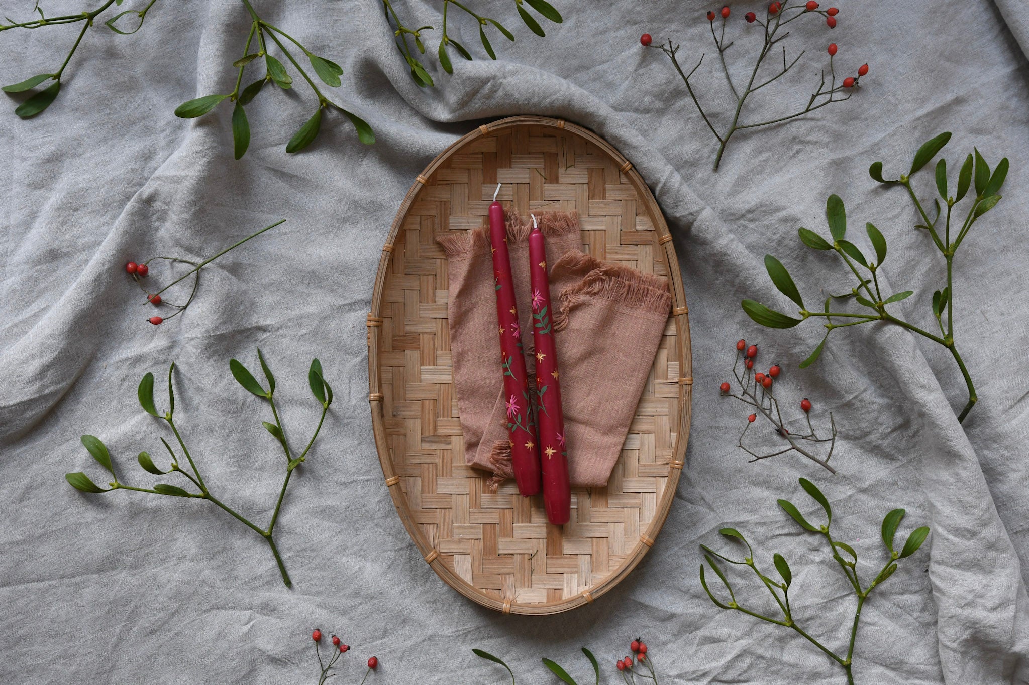 red hand painted winter floral dinner candles in basket surrounded by mistletoe